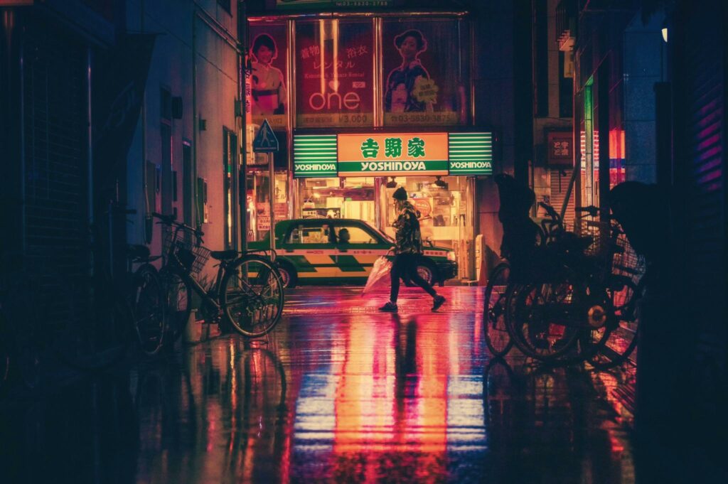 Atmospheric night cityscape featuring neon lights, wet streets, and urban life in Tokyo.