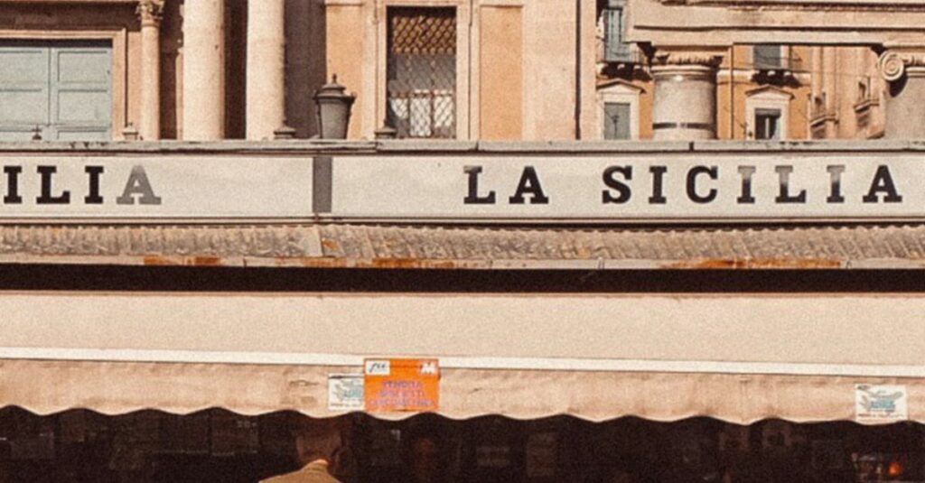 Roadtrip en Sicile : Itinéraire de 1 semaine 🇮🇹 Charming Sicilian street scene with a kiosk, scooter, and historic architecture.
