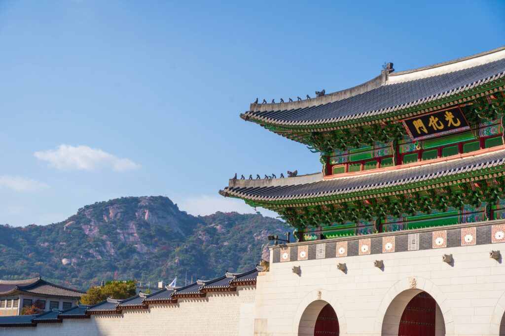Temples et palais à Séoul : culture, histoire et immersion 🇰🇷 View of Gyeongbokgung Palace with traditional Korean architecture set against a mountain backdrop on a sunny day.