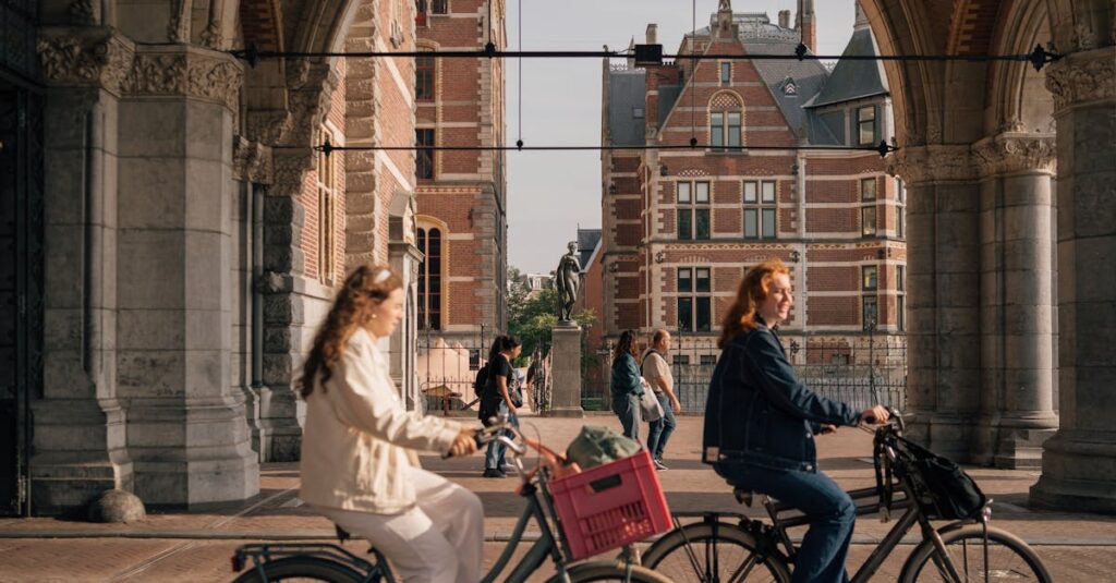 Women cycling under an Amsterdam archway with historical buildings in the background.